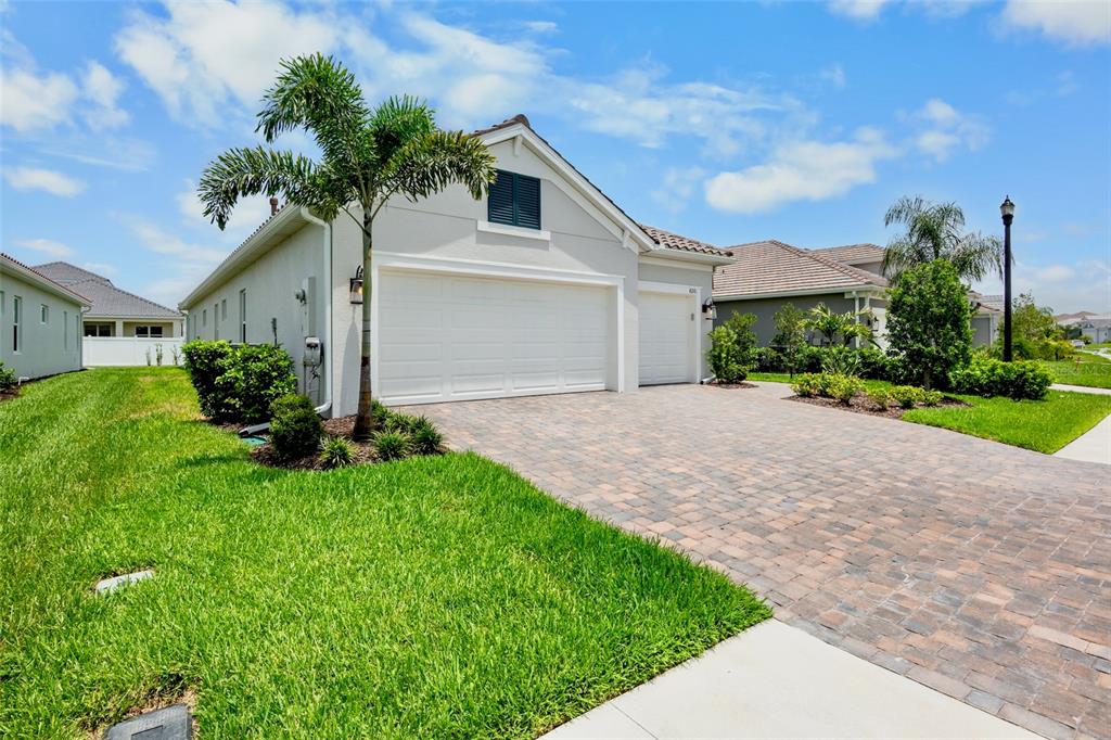 A light-colored house exterior features a paved driveway, a palm tree, and a three-car garage — 8091 ANTHIRIUM LOOP, SARASOTA, FL