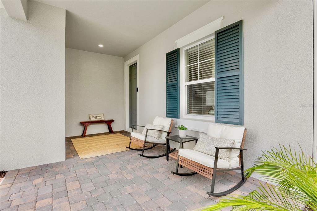 A covered front porch features a brick paver floor, two rocking chairs, and a small bench — 8091 ANTHIRIUM LOOP, SARASOTA, FL