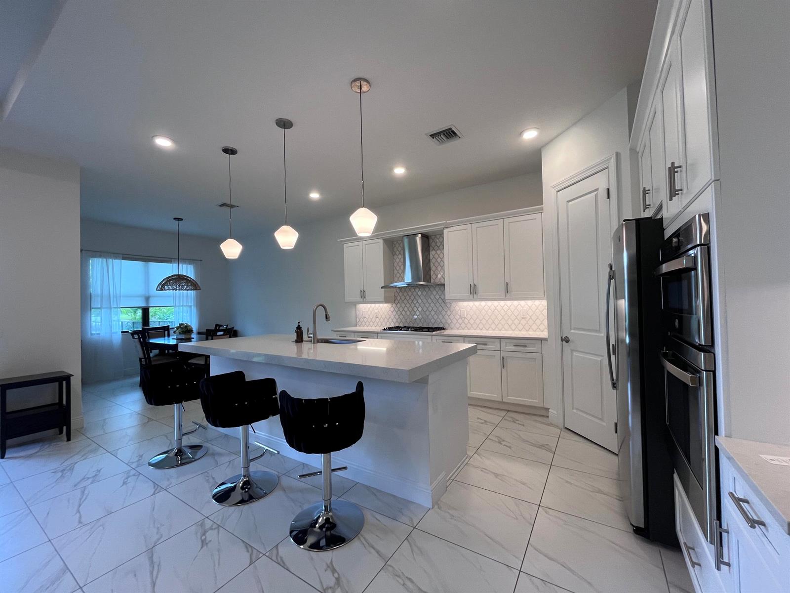 A modern white kitchen features a large island, stainless steel appliances, and marble-look tile flooring — 5663 Saint Armands Way, FL 33470, FL