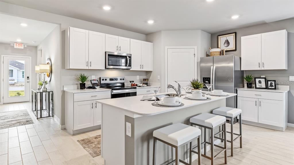 A modern kitchen features white cabinets, a central island with bar stools, and stainless appliances — 26263 CORAL LAKES DRIVE, PUNTA GORDA, FL