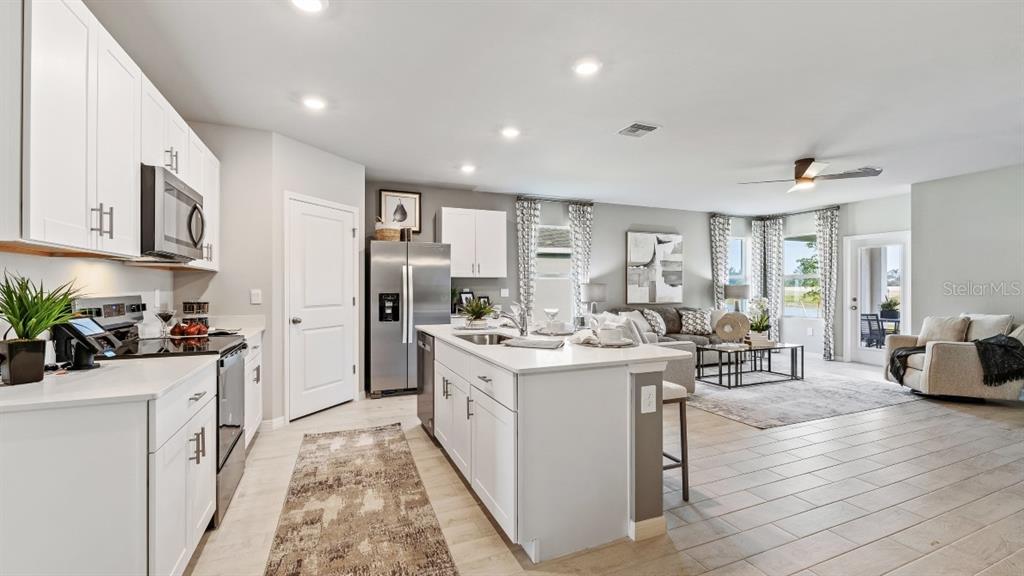 A bright open-concept kitchen and living area features white cabinetry, quartz countertops, and tile flooring — 26263 CORAL LAKES DRIVE, PUNTA GORDA, FL