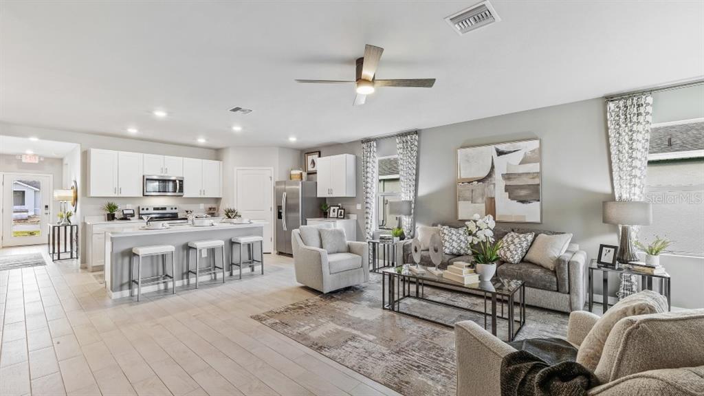 An open-concept living room and kitchen feature white cabinetry, light tile flooring, and neutral furniture — 26263 CORAL LAKES DRIVE, PUNTA GORDA, FL
