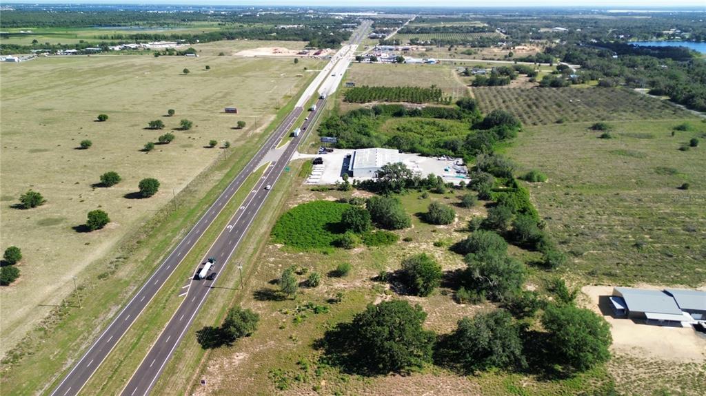 An aerial view shows a highway running past a commercial building and surrounding rural land — US HWY 27, SEBRING, FL