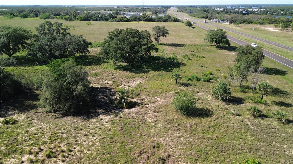An aerial view shows a large, grassy, undeveloped lot with scattered trees near a highway — US HWY 27, SEBRING, FL