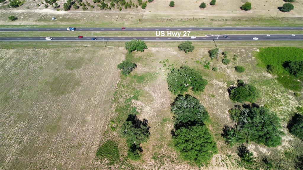 An aerial view shows a vacant, tree-dotted lot adjacent to a multi-lane highway — US HWY 27, SEBRING, FL
