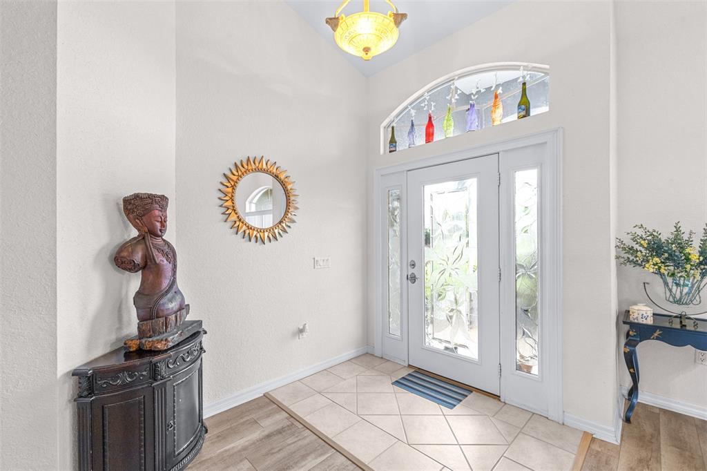 A foyer features a tiled entryway, a decorative statue, a sunburst mirror, and a glass-paneled door — 6546 BENDELOW DRIVE, LAKELAND, FL