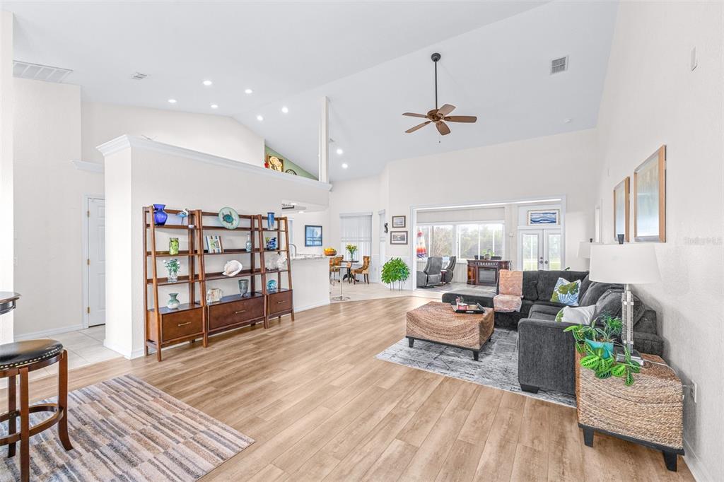 A spacious living room features vaulted ceilings, wood-look flooring, and an open-concept layout — 6546 BENDELOW DRIVE, LAKELAND, FL