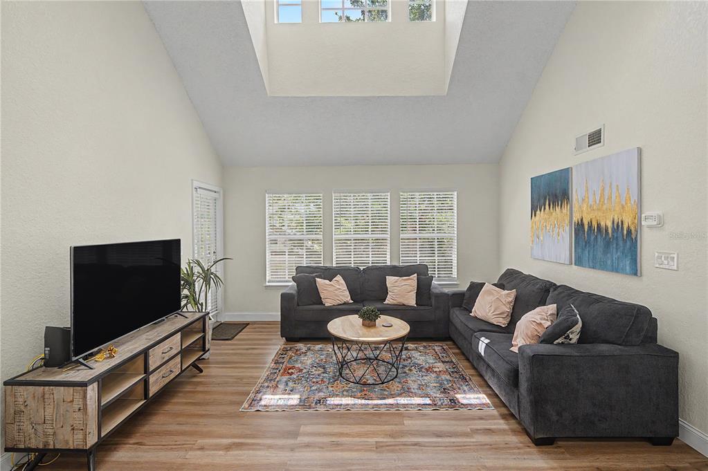 A living room features a vaulted ceiling, wood-look flooring, a sectional sofa, and a television — 3266 HAVILAND COURT UNIT 303, PALM HARBOR, FL