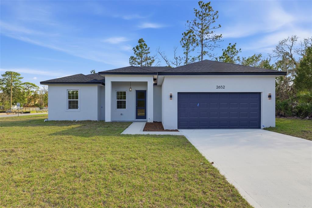 A single-story house with white stucco walls, a dark roof, and a blue garage door — 2652 W PARAGON LANE, DUNNELLON, FL