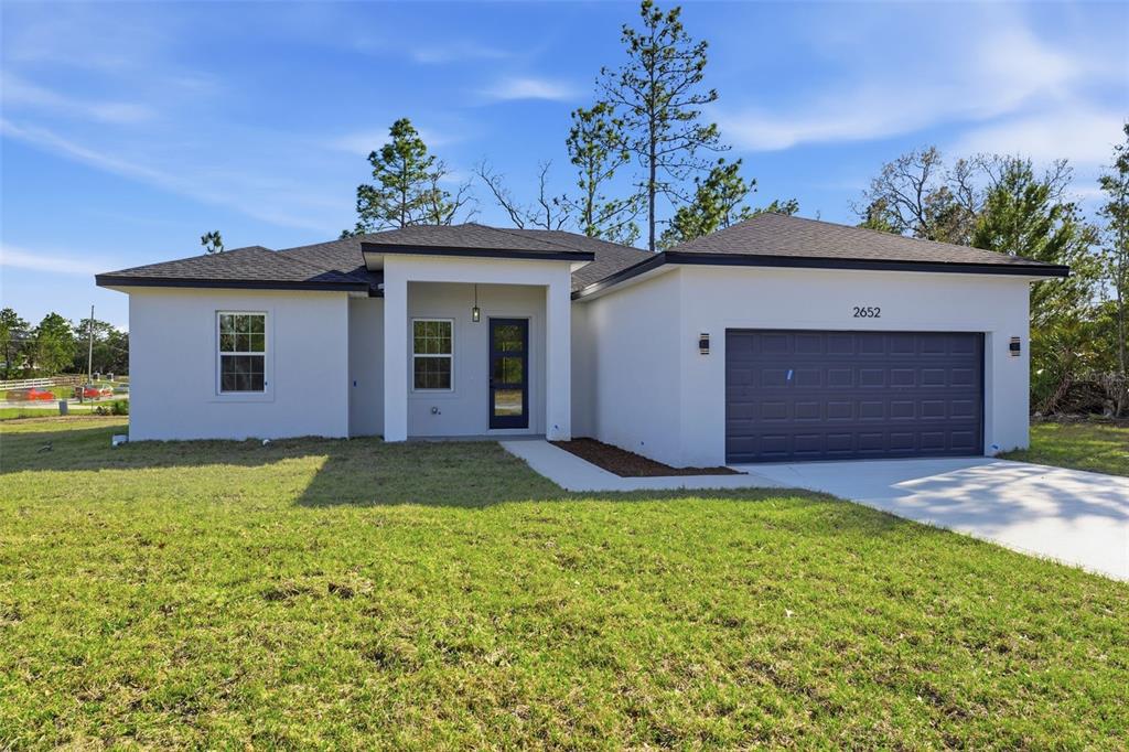 A single-story house with white stucco walls, a dark roof, and a two-car garage — 2652 W PARAGON LANE, DUNNELLON, FL