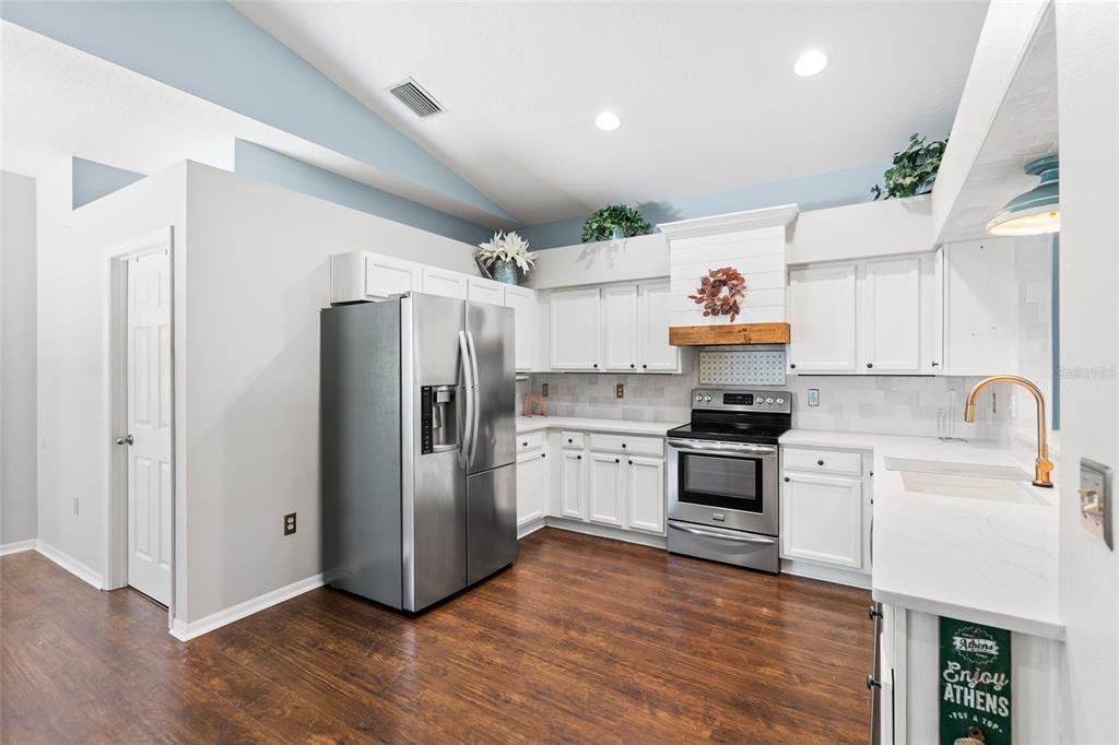 A kitchen with white cabinets, stainless steel appliances, and dark wood flooring under a vaulted ceiling — 19218 SEA MIST LANE, LUTZ, FL
