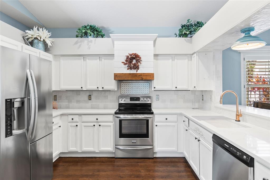 A kitchen features white cabinets, stainless steel appliances, a wood range hood, and white countertops — 19218 SEA MIST LANE, LUTZ, FL
