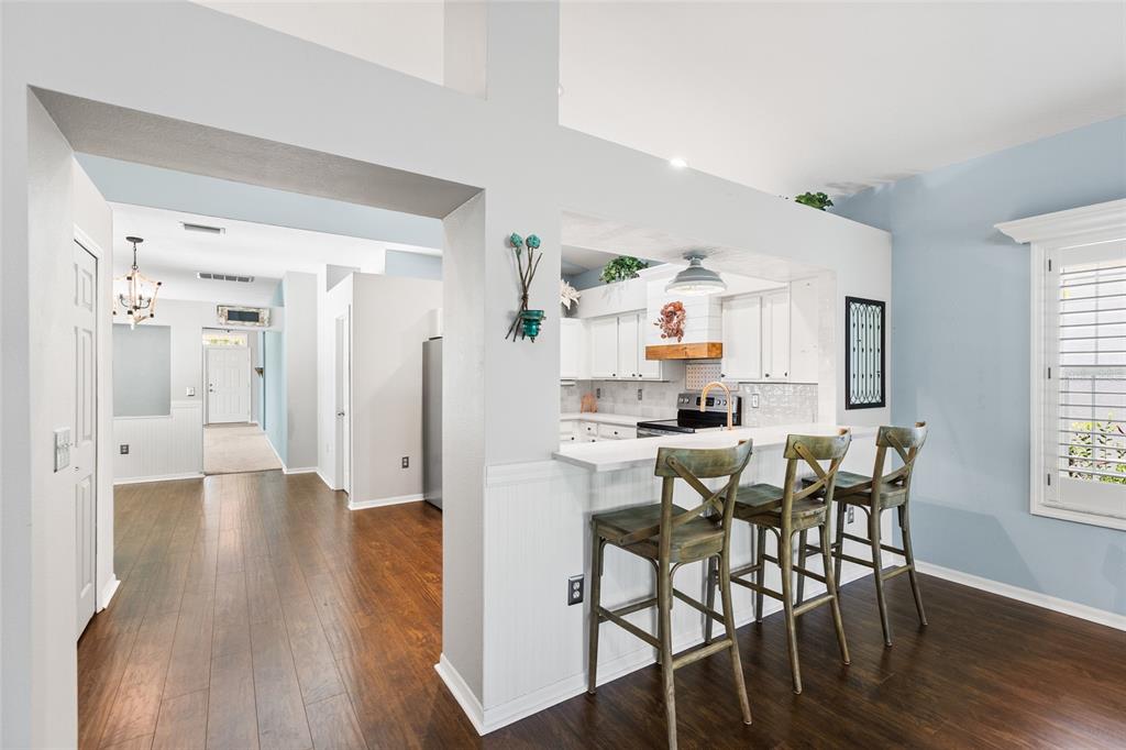 A kitchen with a breakfast bar and three wooden stools opens into a dining area — 19218 SEA MIST LANE, LUTZ, FL