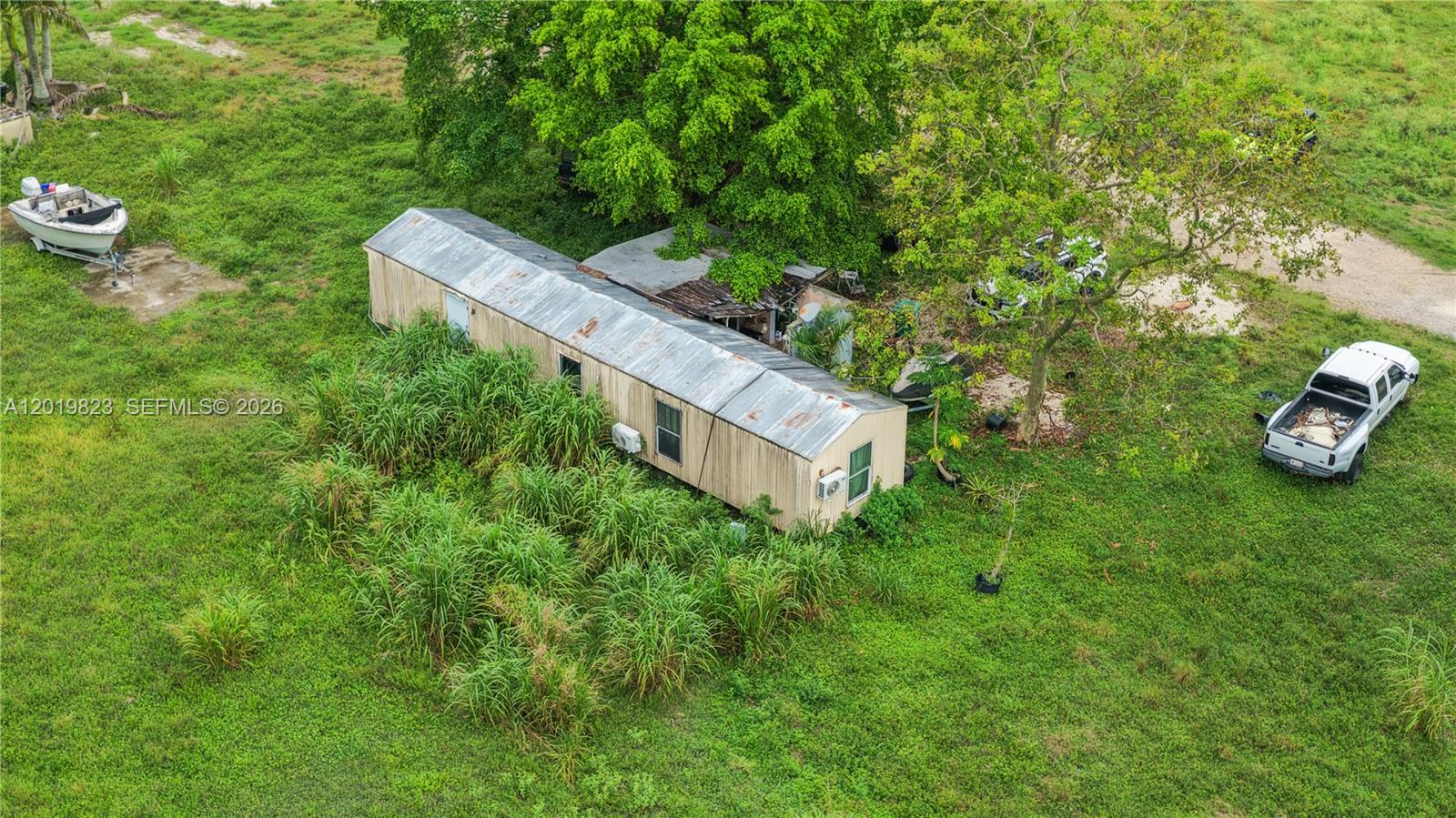 An aerial view shows a mobile home surrounded by tall grass, trees, and vehicles — UNINCORPORATED DADE COUNTY, FL