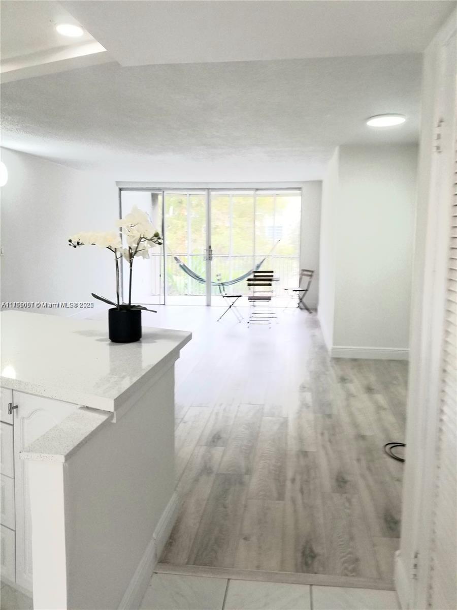 A bright living area features light wood-look flooring, a kitchen island, and a balcony entrance — 1670 NE 191st St # 3, Miami FL 33179, MIAMI, FL