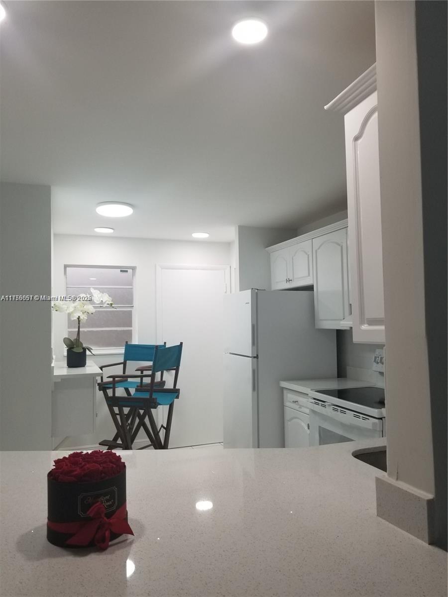 A kitchen features white cabinetry, a refrigerator, a stove, and a small dining area — 1670 NE 191st St # 3, Miami FL 33179, MIAMI, FL