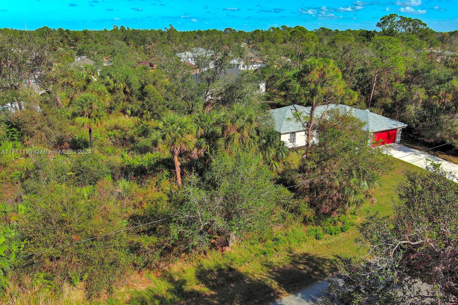 An aerial view shows a single-story house with a red garage door amidst dense vegetation — #2 Sargon Ave, North Port FL 34287, NORTH PORT, FL