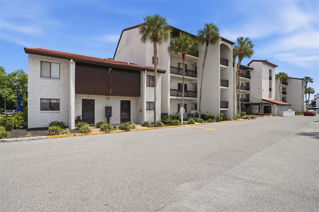 A multi-story apartment building with stucco walls, balconies, and palm trees in a parking lot — 1624 STICKNEY POINT ROAD UNIT 1624-208, SARASOTA, FL