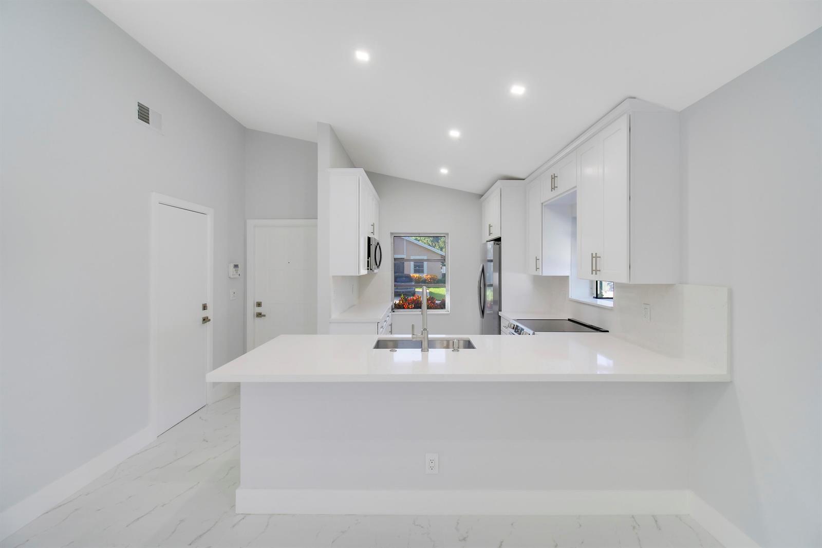 A modern kitchen features white cabinets, quartz countertops, a breakfast bar, and light-colored flooring — 8055 Sweetbriar Way, Boca Raton FL 33496, BOCA RATON, FL