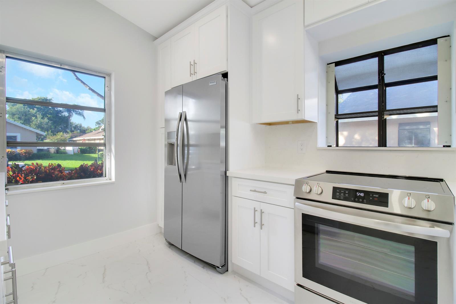A kitchen features white cabinets, stainless steel appliances, marble-look flooring, and two windows — 8055 Sweetbriar Way, Boca Raton FL 33496, BOCA RATON, FL
