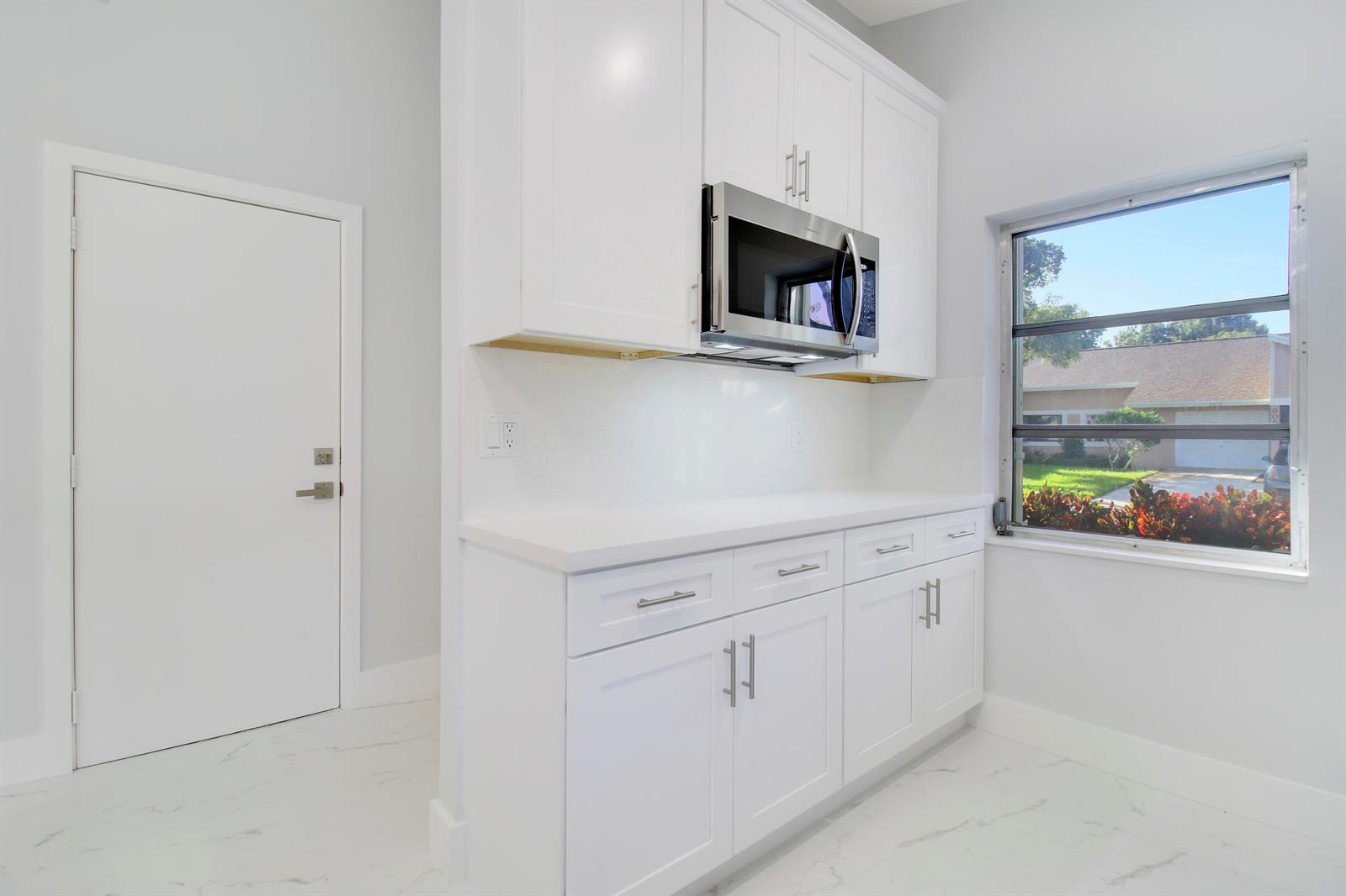 A white kitchen features shaker cabinets, a built-in microwave, quartz countertops, and marble-look flooring — 8055 Sweetbriar Way, Boca Raton FL 33496, BOCA RATON, FL