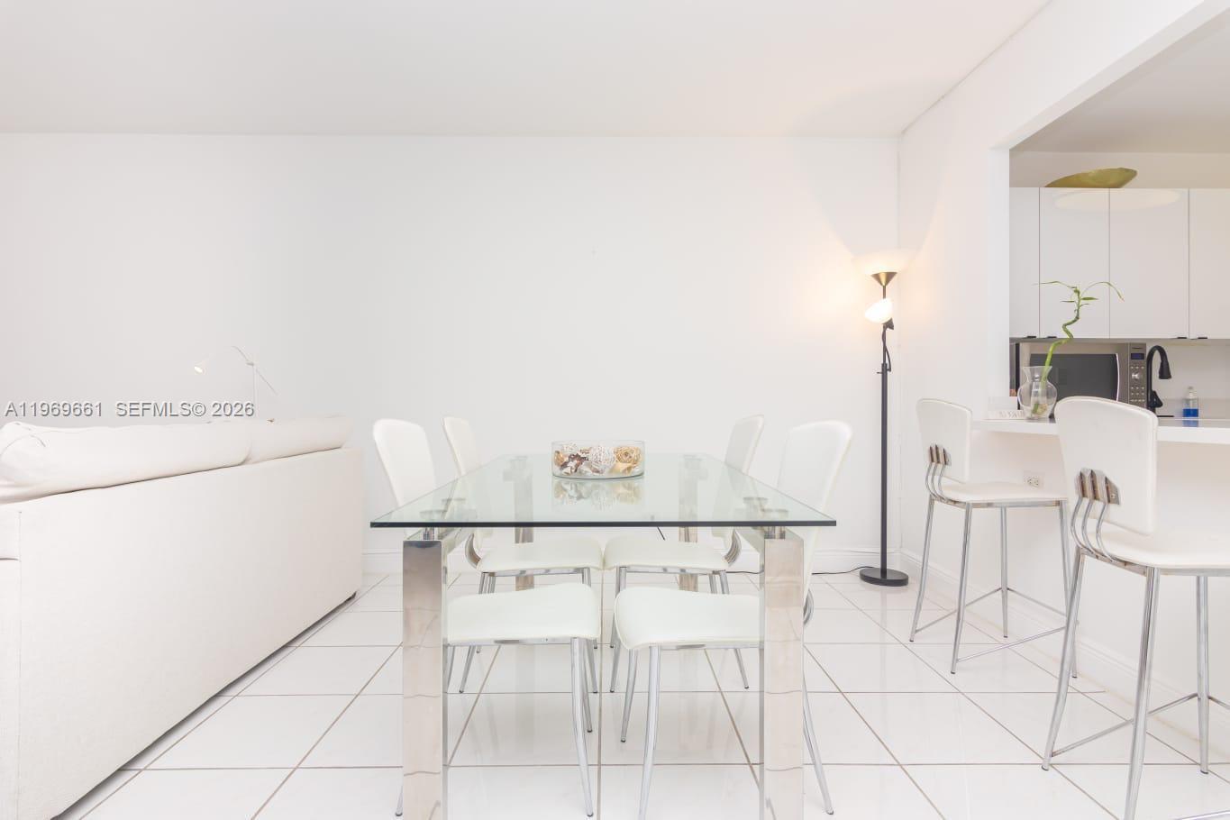 A dining area features a glass table with white chairs and white tile flooring — 2301 Collins Ave # 423, Miami FL 33139, MIAMI, FL