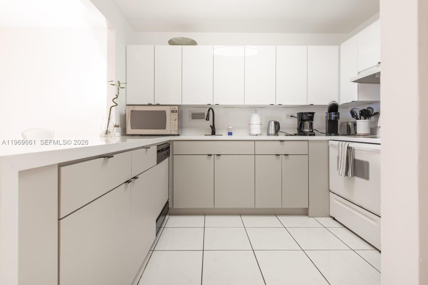 A modern kitchen features white upper cabinets, light gray lower cabinets, and white tile flooring — 2301 Collins Ave # 423, Miami FL 33139, MIAMI, FL