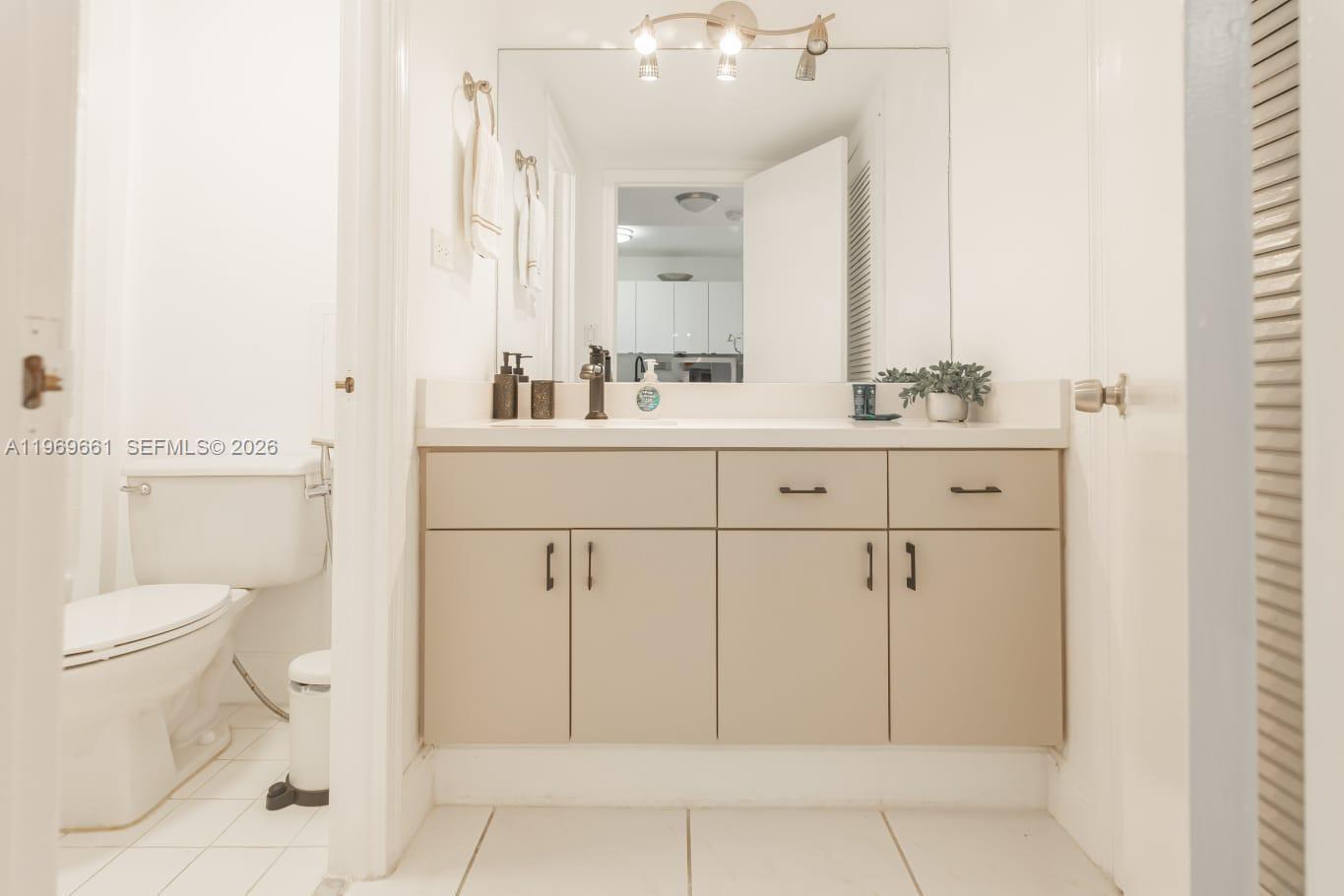 A bathroom features a beige vanity with a white countertop, mirror, and adjacent toilet — 2301 Collins Ave # 423, Miami FL 33139, MIAMI, FL