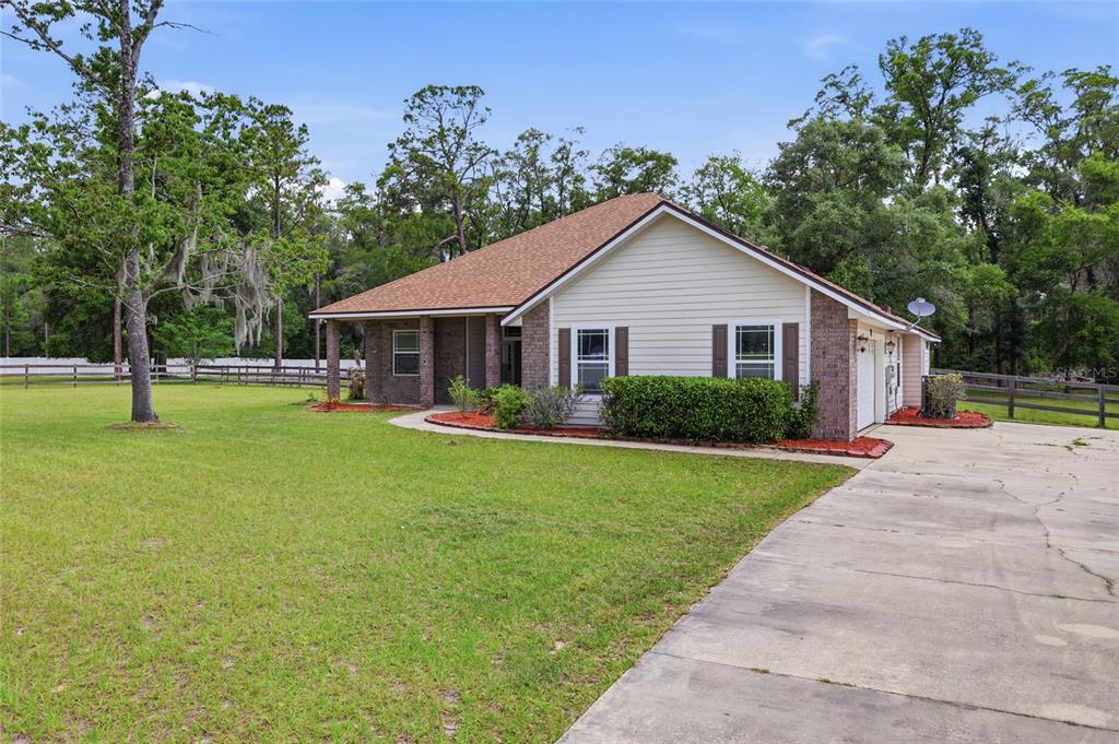 A single-story house with tan siding, brick accents, and a concrete driveway sits on grass — 25176 NW 209TH AVENUE, HIGH SPRINGS, FL