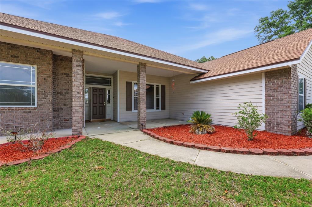 A single-story house exterior features a brick and beige siding facade with a covered porch — 25176 NW 209TH AVENUE, HIGH SPRINGS, FL