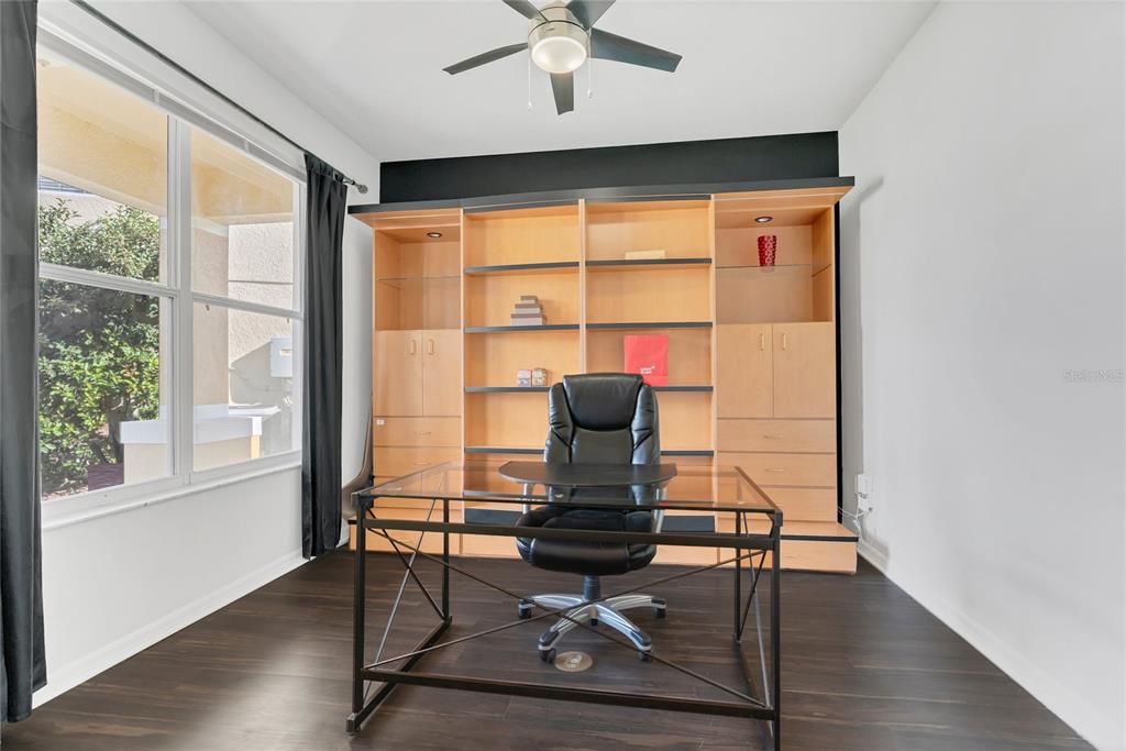 A home office features dark wood floors, a glass desk, and a large built-in bookshelf — 9531 OSPREY LANDING DRIVE, ORLANDO, FL