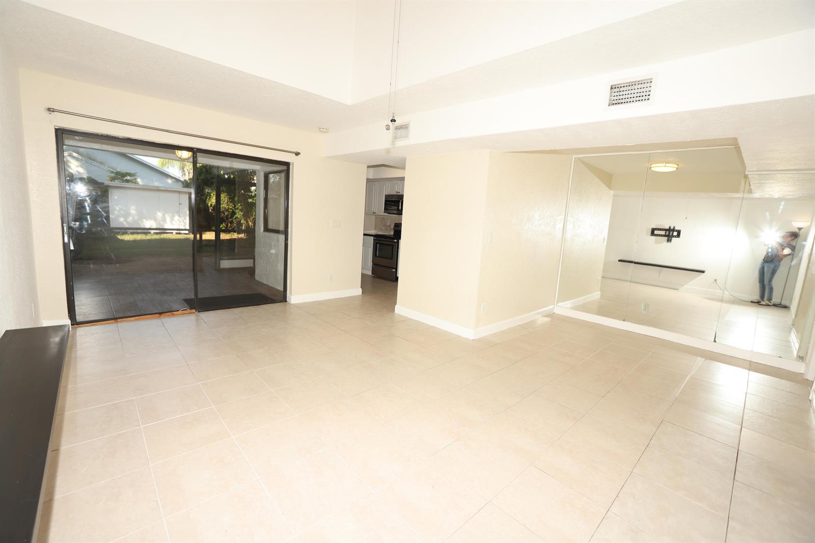 A living room with tile flooring, a sliding glass door, and a mirrored accent wall — 1265 The 12th Fairway, Wellington FL 33414, WELLINGTON, FL