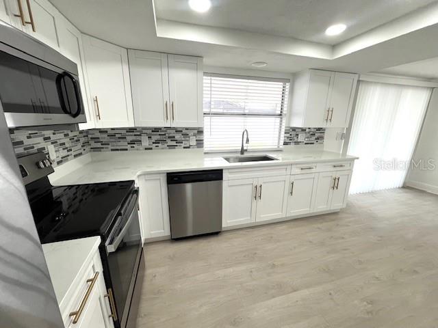 A modern kitchen features white cabinets, stainless steel appliances, and light wood-look flooring — 6646 ALBEMARLE PARKWAY, NEW PORT RICHEY, FL