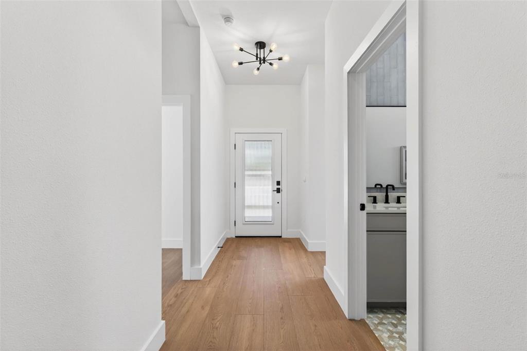 A hallway with light wood floors leads to a white front door under a chandelier — 4365 IRIS STREET N, ST PETERSBURG, FL