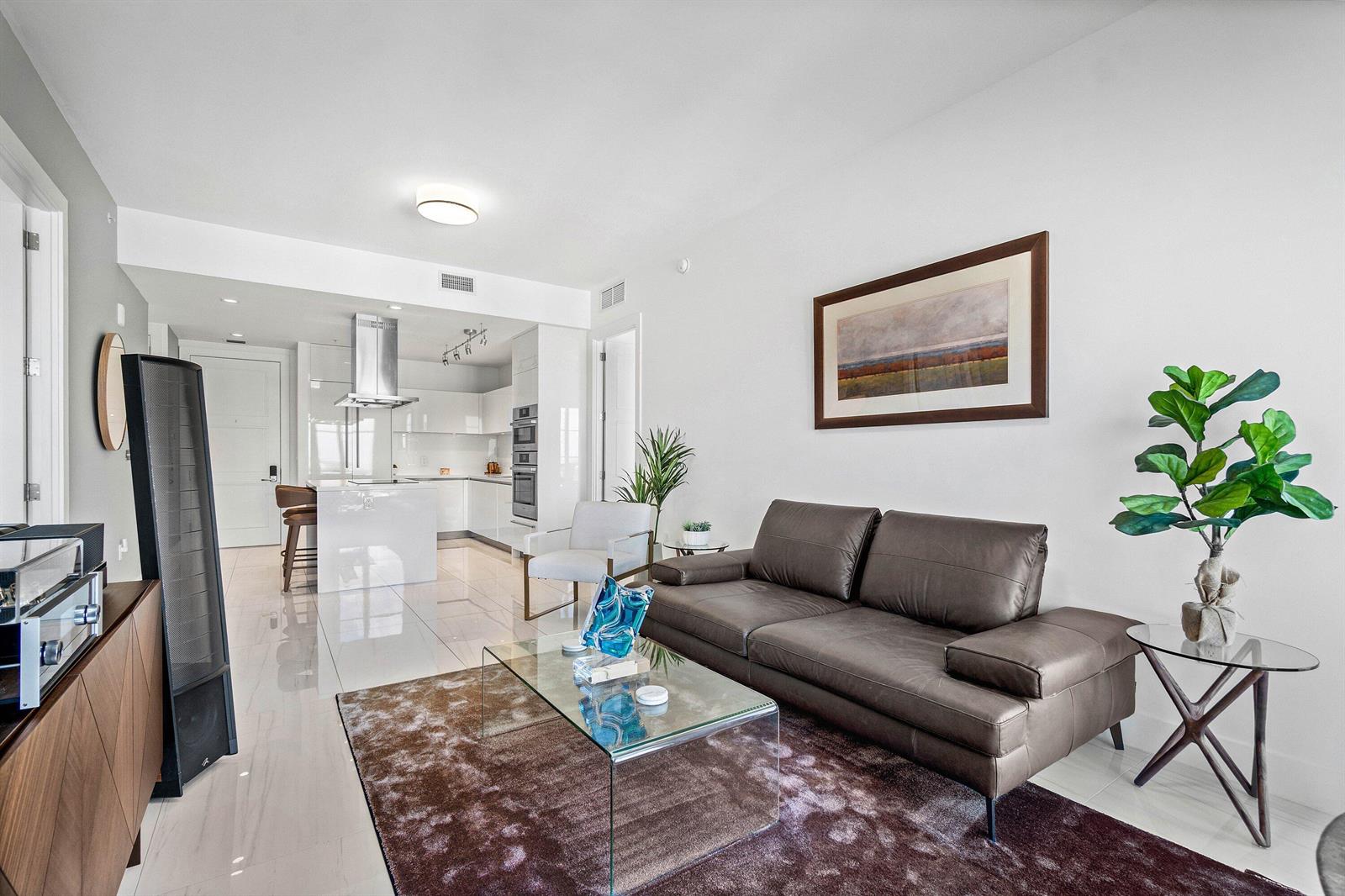 A modern living room with a brown sofa, glass coffee table, and open-concept kitchen — 155 E Boca Raton Road # 1119, Boca Raton FL 33432, BOCA RATON, FL
