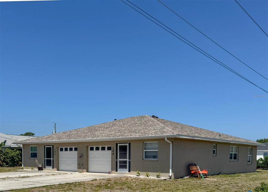A single-story duplex with two garage doors and a tan stucco exterior under a clear sky — 100 CHARLES DRIVE, NOKOMIS, FL