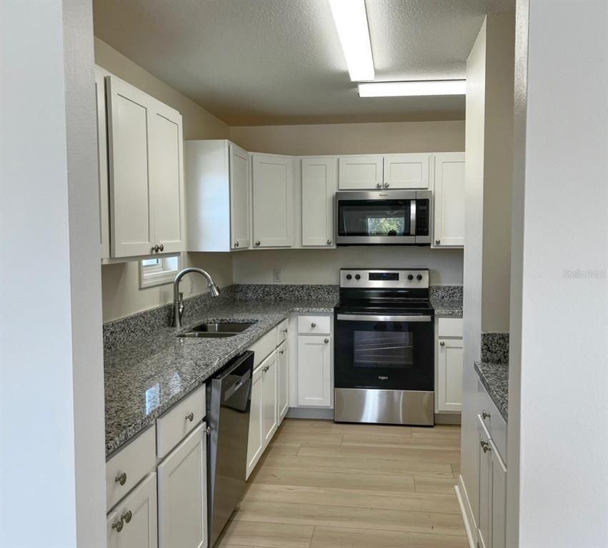 A galley kitchen features white cabinets, granite countertops, and stainless steel appliances — 100 CHARLES DRIVE, NOKOMIS, FL