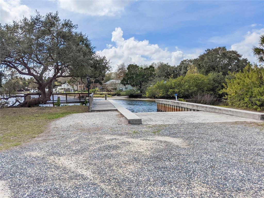 A gravel boat ramp leads into a waterway next to a wooden dock and trees — 1805 MOUNTAIN ASH WAY, TRINITY, FL