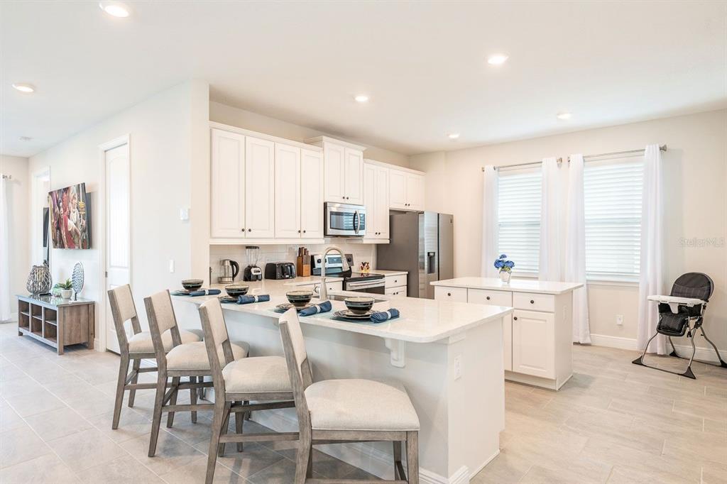 A bright kitchen features white cabinetry, a quartz-topped island with seating, and light tile flooring — 428 SOUTHFIELD STREET, KISSIMMEE, FL