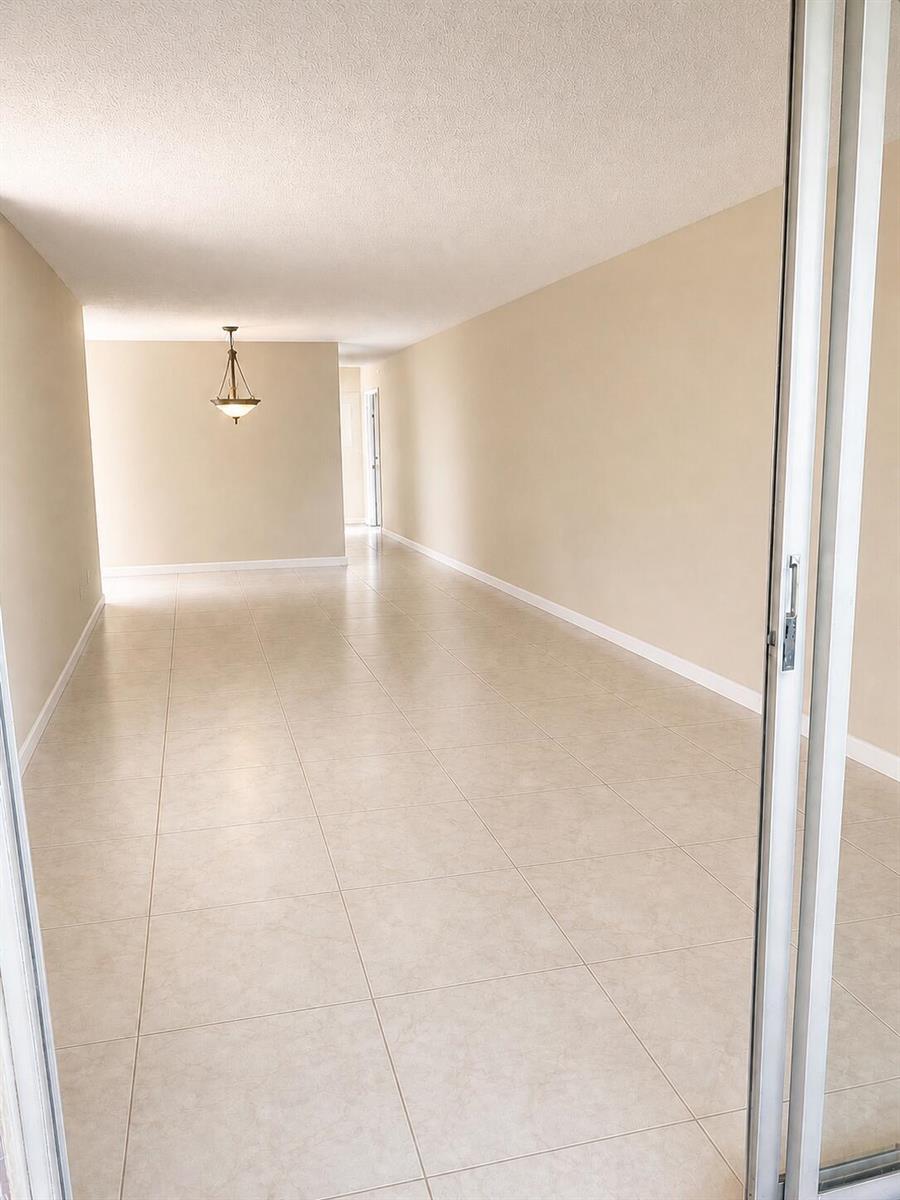 An empty room with beige walls, tile flooring, and a hanging light fixture — 4037 Guildford C, Boca Raton FL 33434, BOCA RATON, FL