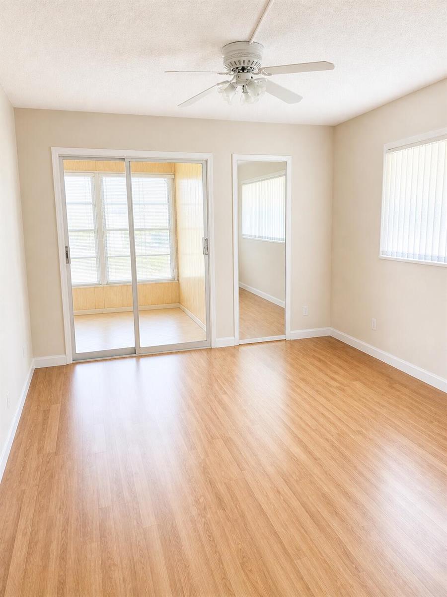 An empty bedroom features light wood-look flooring, a ceiling fan, sliding glass doors, and mirrors — 4037 Guildford C, Boca Raton FL 33434, BOCA RATON, FL