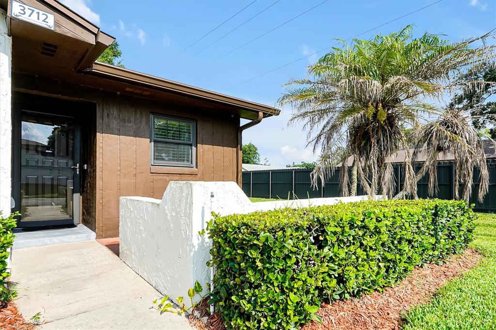 A brown exterior wall with a front door, a window, and a white privacy wall — 3712 BAY COURT, ST CLOUD, FL