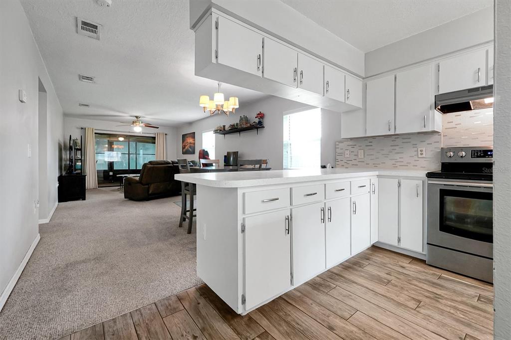 A kitchen with white cabinets and a breakfast bar overlooks a carpeted living area — 3712 BAY COURT, ST CLOUD, FL
