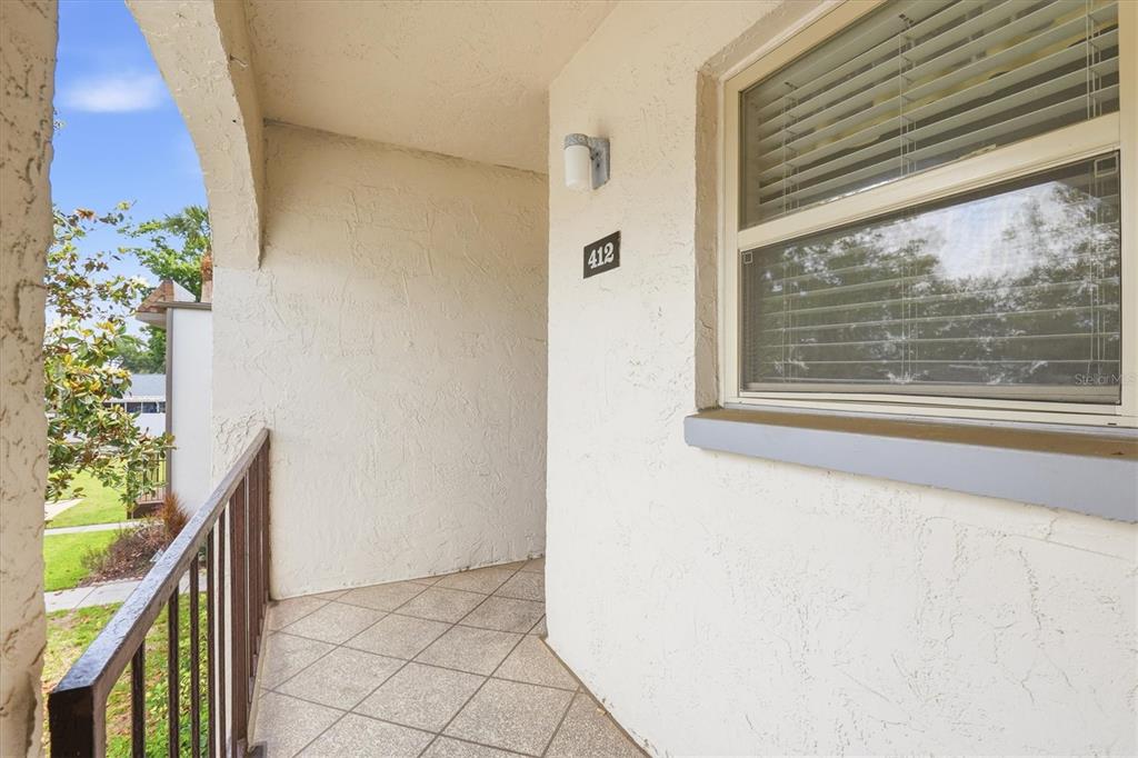 A covered outdoor balcony features tiled flooring, a metal railing, and a window with blinds — 7701 STARKEY ROAD UNIT 412, SEMINOLE, FL