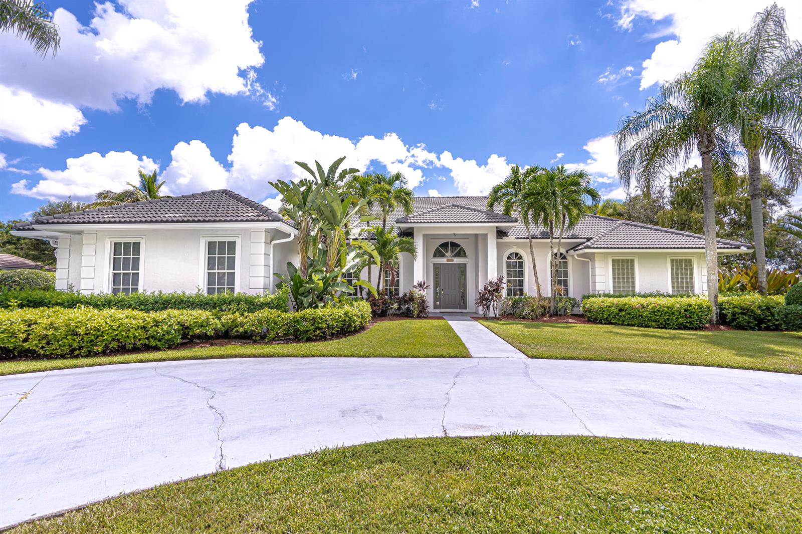 A single-story white house with a tiled roof, palm trees, and a concrete driveway — 15350 Take Off Place, Wellington FL 33414, WELLINGTON, FL