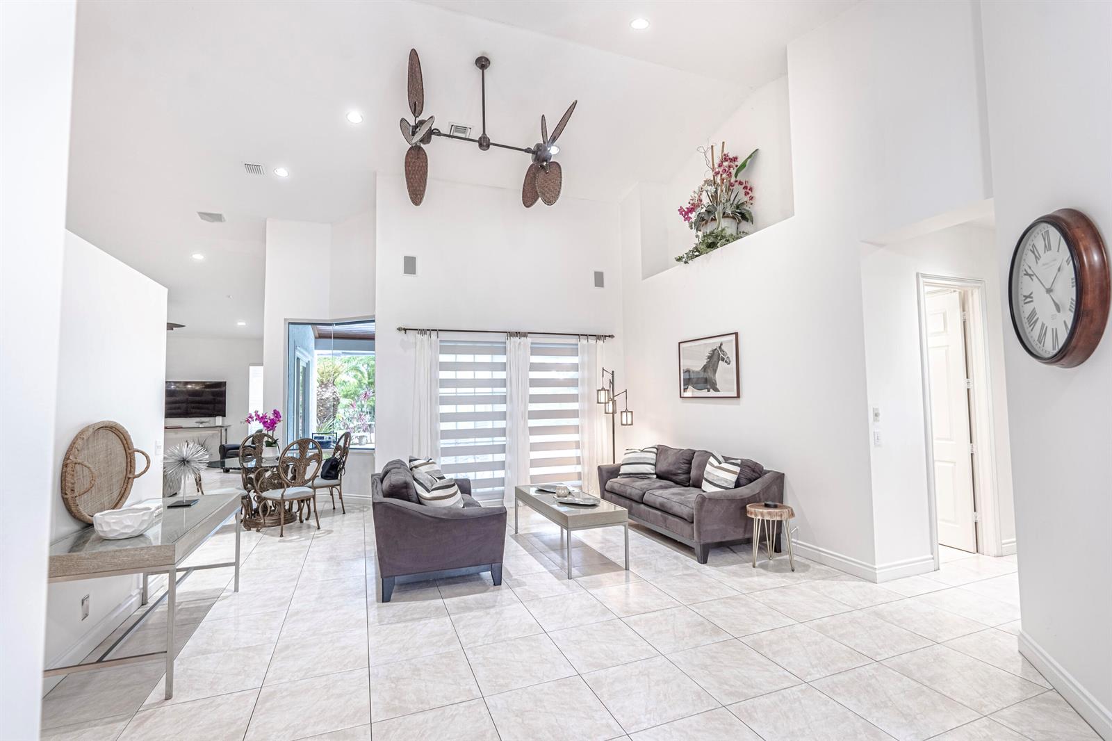 A bright living room features high ceilings, tile flooring, two gray sofas, and a ceiling fan — 15350 Take Off Place, Wellington FL 33414, WELLINGTON, FL