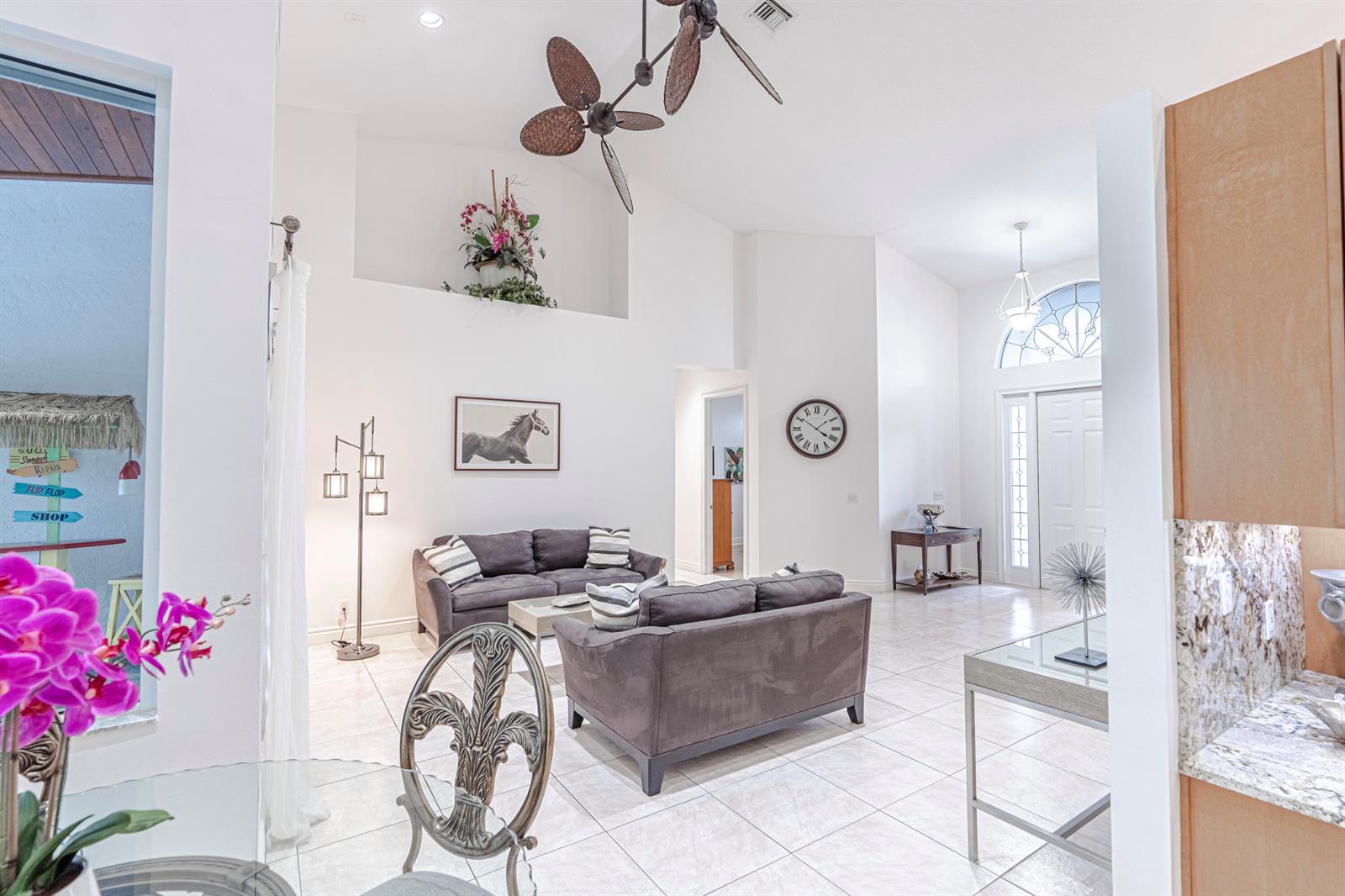 A bright living room features high ceilings, tile flooring, two gray sofas, and a ceiling fan — 15350 Take Off Place, Wellington FL 33414, WELLINGTON, FL