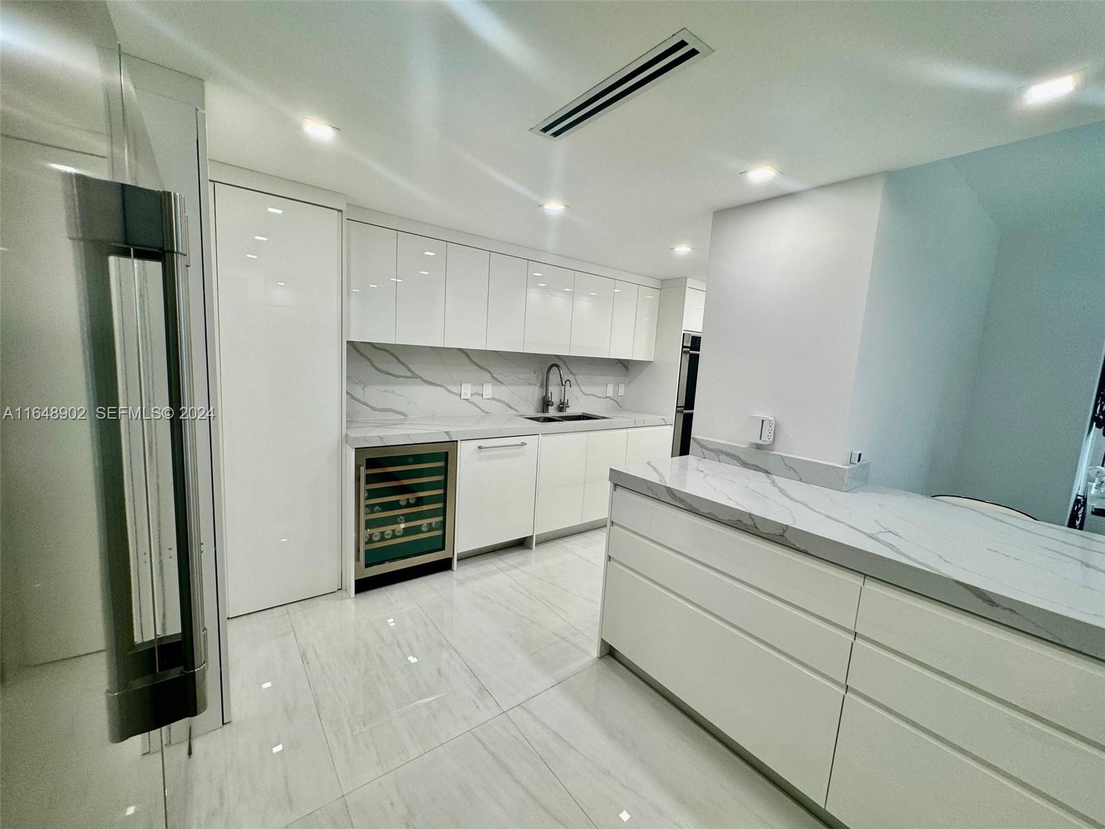 A modern white kitchen features marble-patterned countertops, a wine cooler, and glossy cabinetry — 9801 Collins Ave # 5U, Bal Harbour FL 33154, BAL HARBOUR, FL