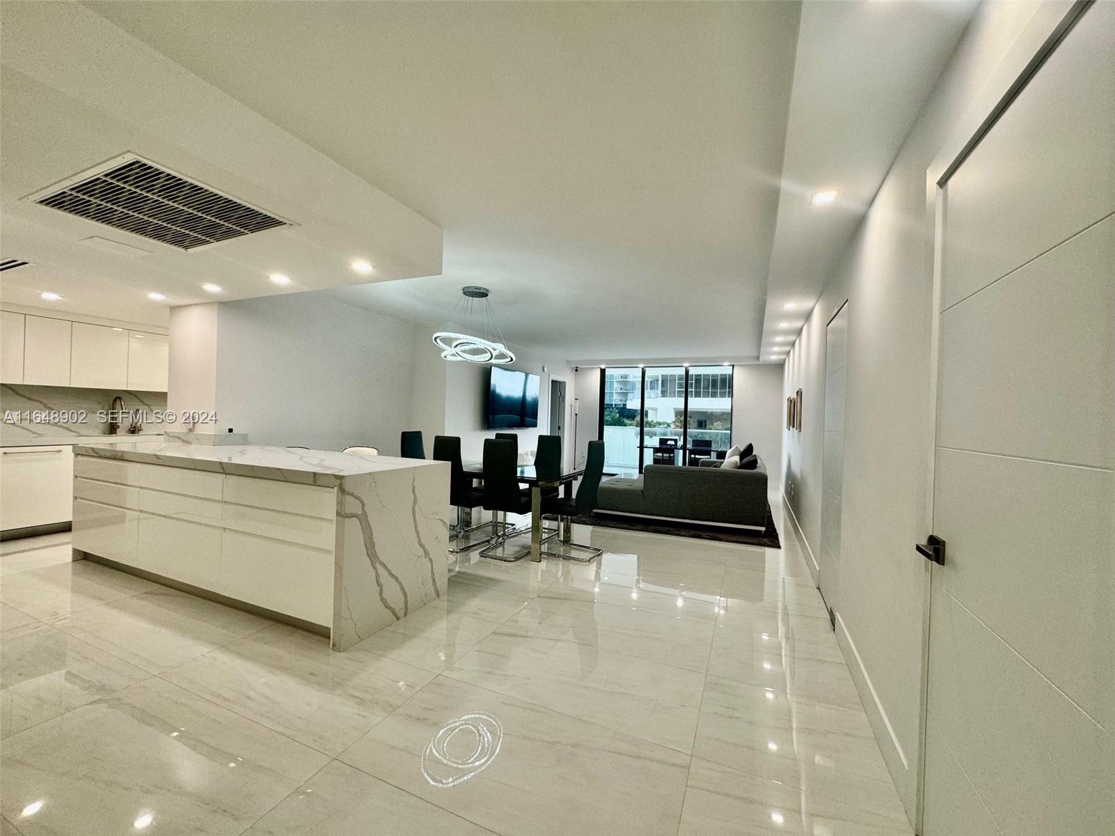 A modern open-plan living area features a marble kitchen island, dining set, and balcony access — 9801 Collins Ave # 5U, Bal Harbour FL 33154, BAL HARBOUR, FL