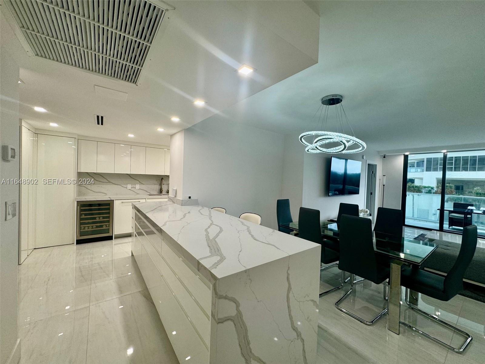 A modern kitchen and dining area feature white marble countertops, glossy cabinets, and tile flooring — 9801 Collins Ave # 5U, Bal Harbour FL 33154, BAL HARBOUR, FL